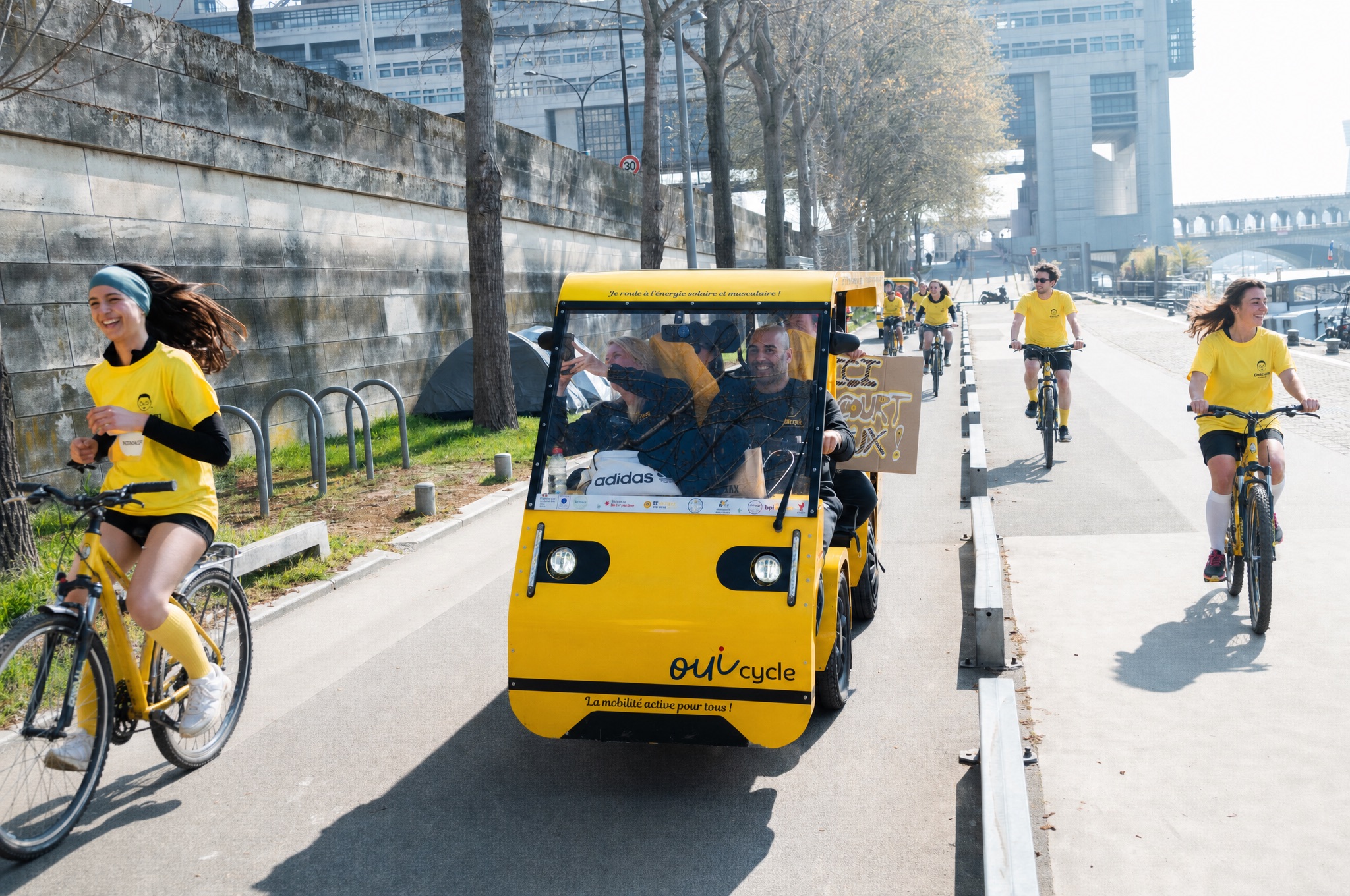 Le OuiCycle roule sur les quais de Seine, entouré de cyclistes en maillot jaune